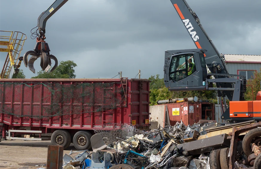 atlas long reach with grab attachment moving scrap metal into a lorry container